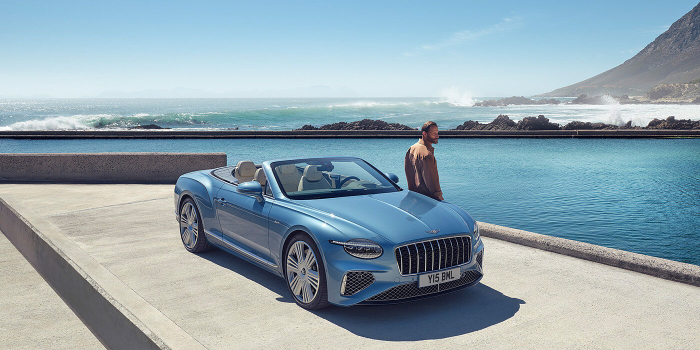 Bentley Yerevan New Bentley Continental GTC Azure convertible front view in Light Windsor blue paint with 22 inch ten spoke wheels parked by the sea in the sunshine