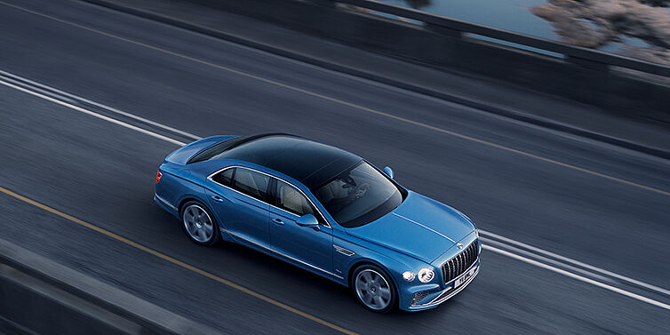 Bentley Yerevan New Bentley Flying Spur Azure sedan in Light windsor blue paint by Mulliner, with 22 inch Azure wheels seen from overhead driving dynamically on a country road