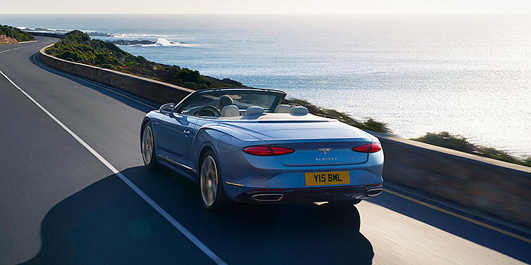 Bentley Yerevan New Bentley Continental GTC Azure convertible rear view in Light Windsor blue paint with 22 inch ten spoke wheels driving dynamically on an ocean road in the sunshine